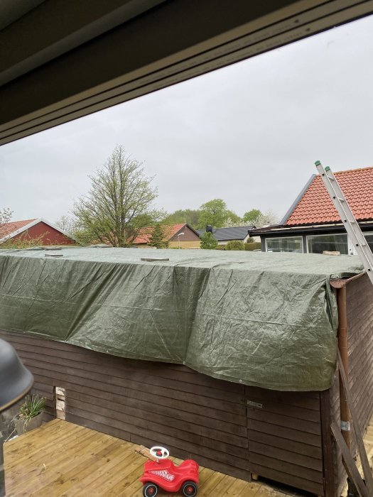 Garagetak under renovering täckt med presenning, synlig stege och sparkbil i förgrunden.