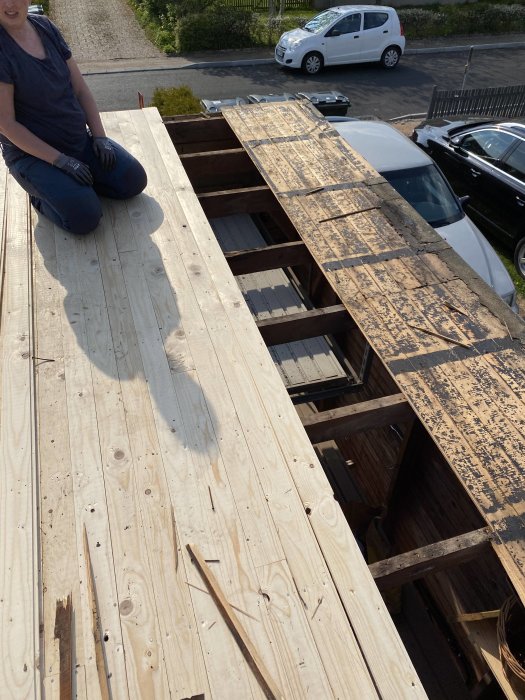 En person som sitter på ett delvis bytt garagetak med nya plankor och öppna sektioner.