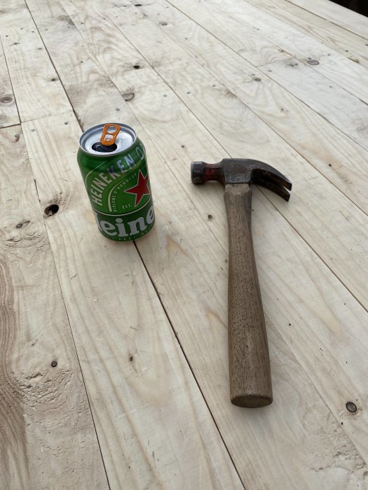 Gamla hammaren bredvid en ölburk på ett nytt trägolv, referens till byggprojekt.