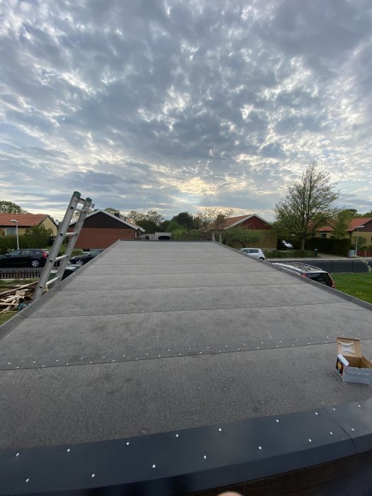 Nytt takmaterial på ett garage mot himmel med moln, stege synlig, byggavfall på marken.