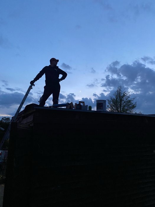 Person står på ett nyligen ombyggt garagetak i silhuett mot en kvällshimmel.