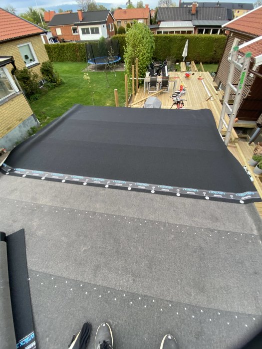 Nytt svart garagetak med synliga spikar och trädgård i bakgrunden, sett ovanifrån.