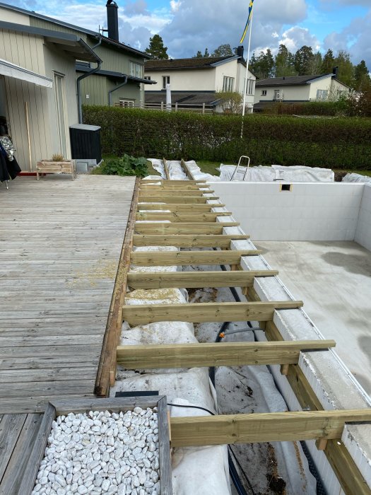 Nyinstallerade träreglar på en byggarbetsplats, intill en pool och ett trädäck, med hus i bakgrunden.