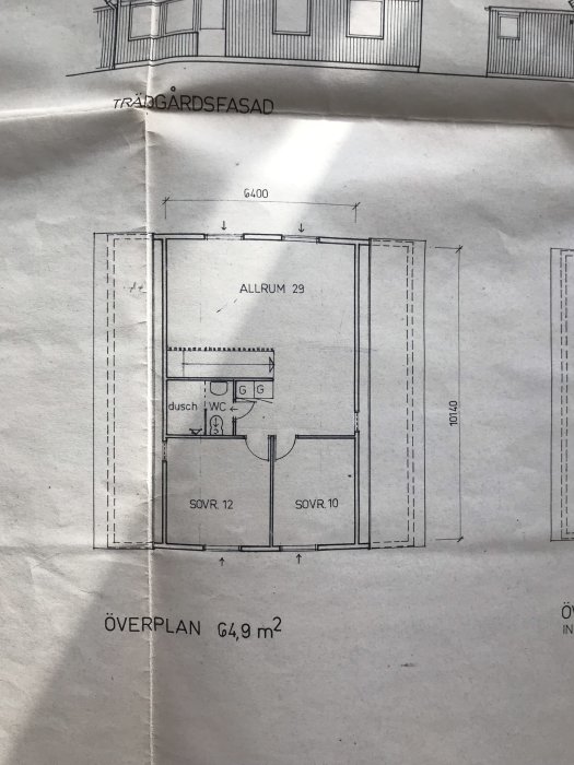 Ritning över övre plan i hus med allrum, WC, dusch och två sovrum, märkt "TRÄDGÅRDSFASAD" och "ÖVERPLAN 64,9 m²".