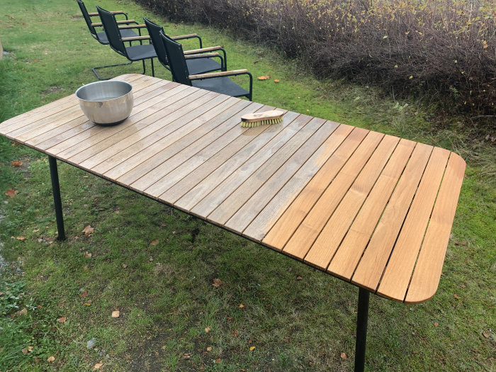 Trädgårdsbord i teak halvt torrt och halvt blött, framhäver färgskillnad, i gräsmiljö.