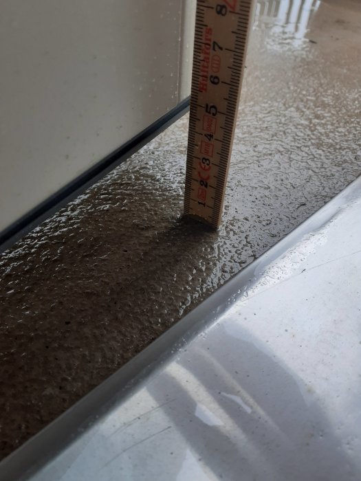 Måttstock visar avståndet mellan balkongdörr och betonggolv, potentiellt utrymme för trall.