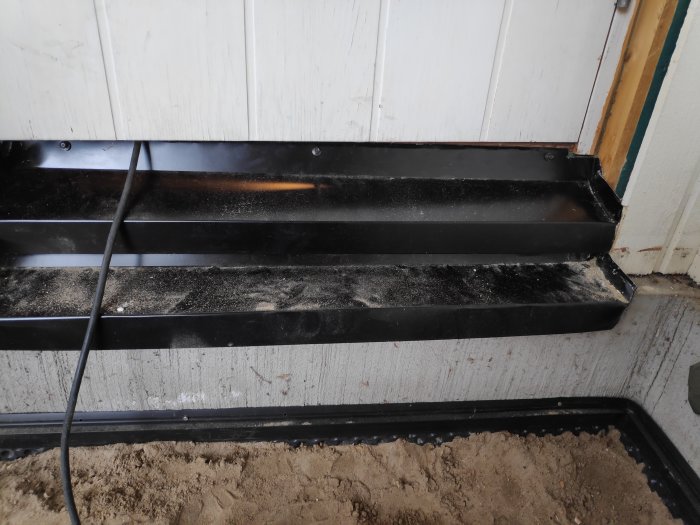 Nyinstallerat svart tröskelbleck vid dörröppning i behov av slutlig fogning.