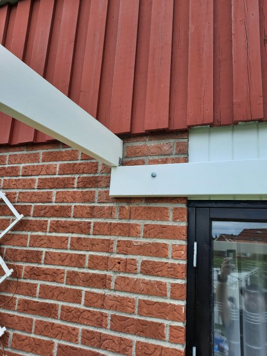 Minimal urjackning vid takfot över en tegelvägg, med vita stuprör och takpanel i rött.