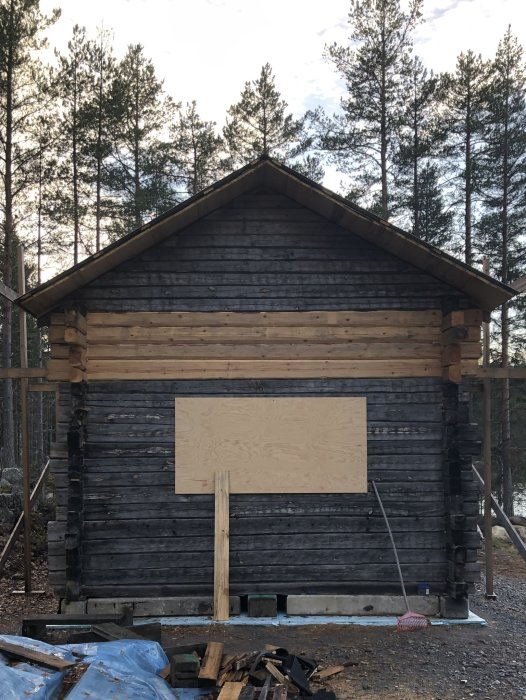 Timrad stuga med nytt virke på nedre delen och äldre, mörkare timmer ovanför, med spår av mögel.