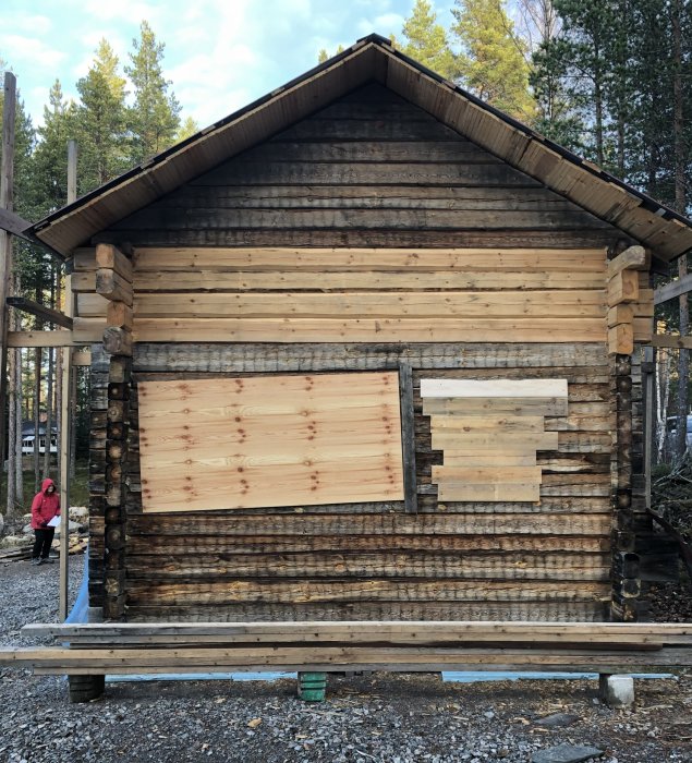 Timrad stuga med synliga mögelfläckar på väggarna och nytt ljust timmer upptill.