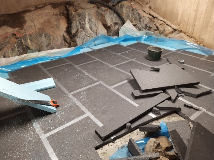 Delvis lagd golvkonstruktion med skumglasblock och isoleringsmaterial, verktyg och avkapade bitar synliga.