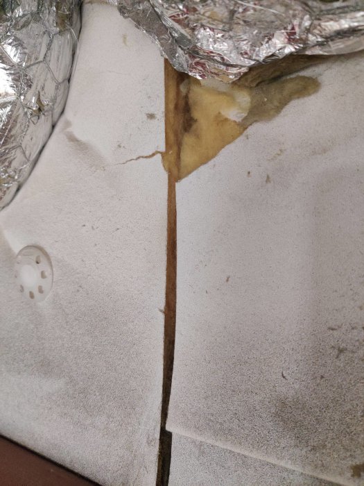 Glas/mineralullsisolering med vitt ytskikt i garage och synlig skada/genomföring.