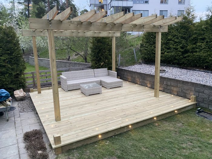 Nybyggd träaltan med pergola och inbyggd belysning, omgiven av trädgård och staket.