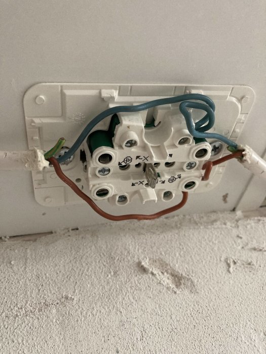 Eluttag utan kåpa visar avklippta jordkablar och delar av installationen mot en vit vägg.
