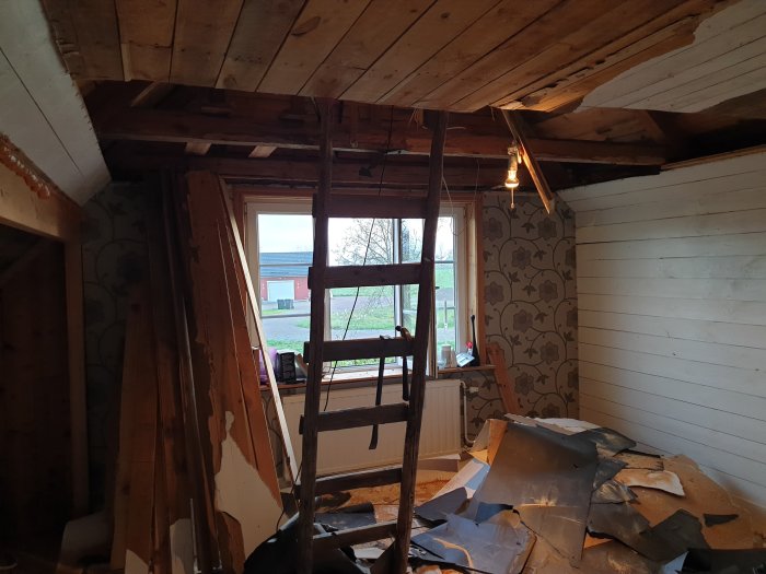 Pågående renovering av ett rum med rivna väggar, en stege och utspridda byggmaterial på golvet.