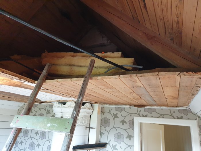 Renovering påbörjad i gammal byggnad med exponerade träbjälkar och stege upp till takutrymme.