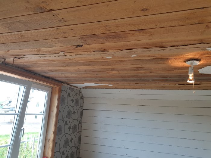 Renoveringsprojekt med påbörjad takbjälklag och vitmålade väggar samt en hängande lampa.