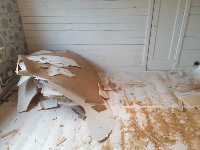 Renoveringsarbete med borttaget gips från vägg och skräp på golvet.