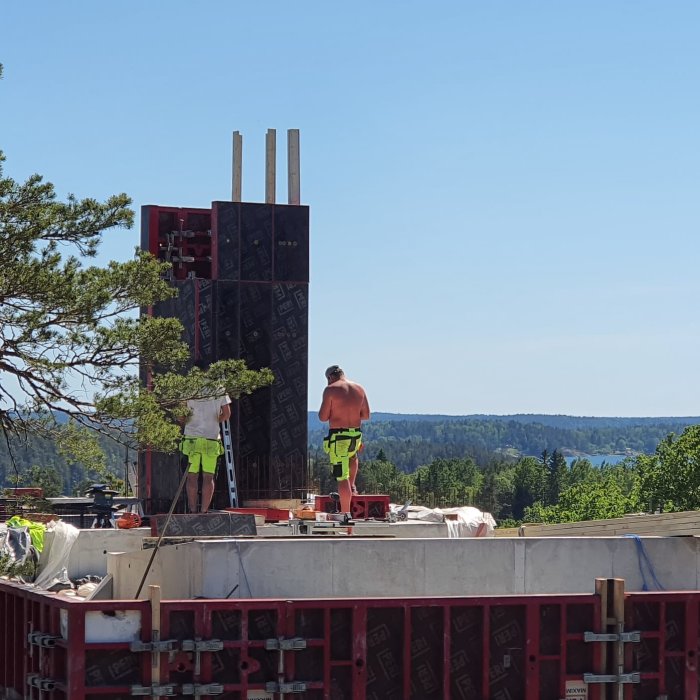 Arbetare bygger en unik huskonstruktion på ett berg med utsikt över vatten.