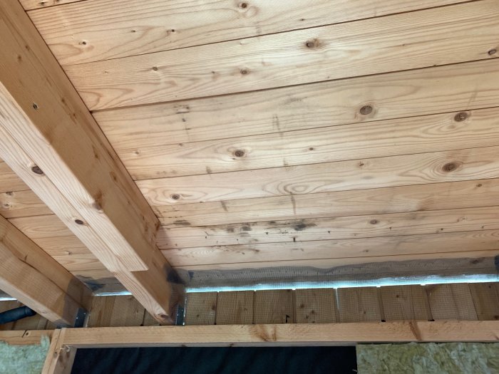Innertak av trä med synliga bjälkar, en smal springa för ventilation och isolering under.
