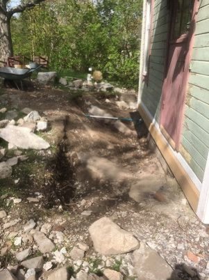 Bergshäll framför en villa med lutning mot huset, planerad plats för farstukvist med grus och jord.