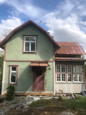 Grön traditionell villa med röd farstukvist och bergshäll i förgrunden som lutar mot huset.