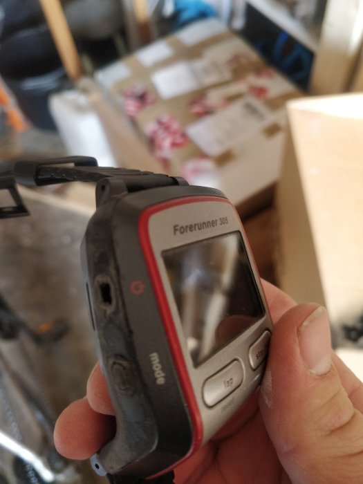 Hand håller en sliten Garmin Forerunner 305 med en trasig knapp.
