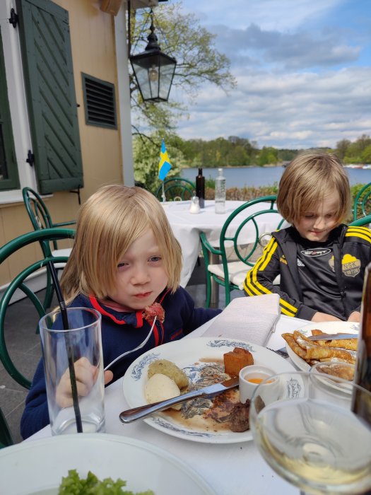 Två barn äter lunch utomhus på Stallmästargården med utsikt över vatten.