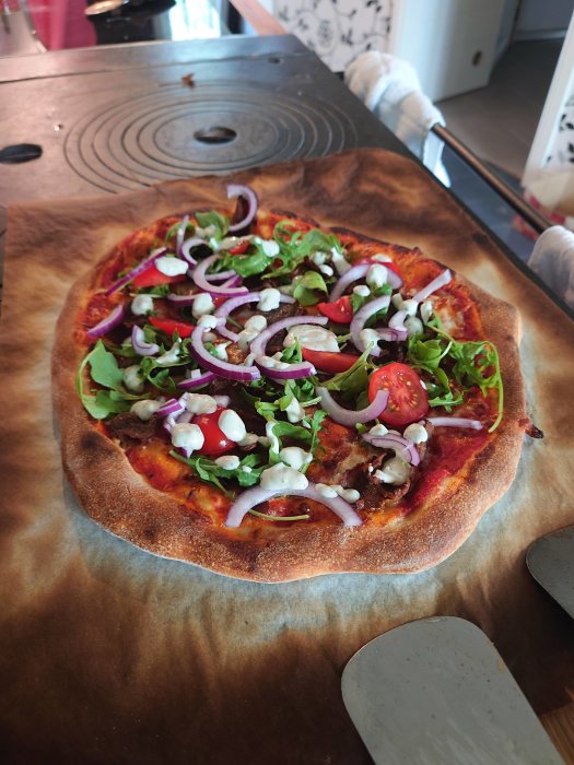 Kebabpizza med sallad, tomat och rödlök på bakplåtspapper, redo att serveras.