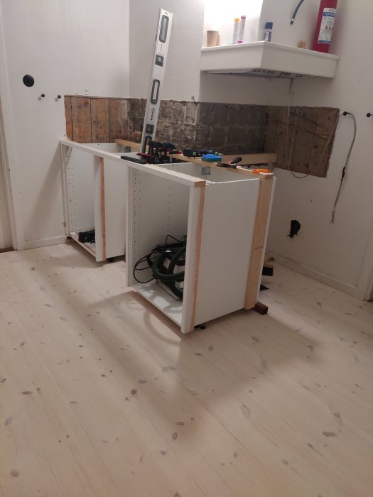 Påbörjad köksrenovering med skåpstommar och verktyg utspridda på trägolvet.