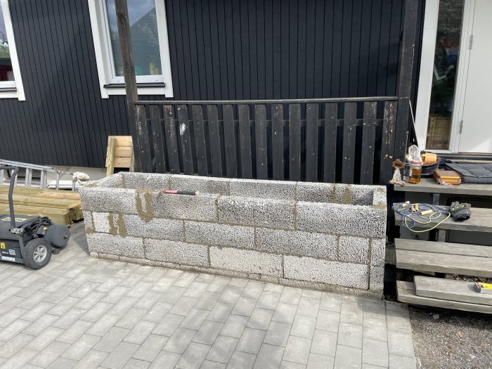 Nybyggd stomme till blomlåda av murblock framför svart trähus och staket.