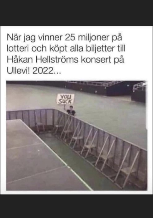 Tomt stadion med en person som håller ett skylt med texten "YOU SUCK" i en humoristisk kontext om en vinst och köp av konsertbiljetter.