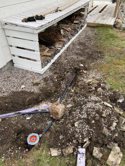 Nedgrävd PEM-slang för Gardena Pipeline vid en husgrund med vedstapel ovanpå.