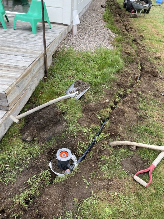 Installation av Gardena Pipeline i grävd ränna i trädgården med verktyg synliga.