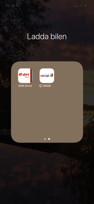 Mobilskärm med två appar för att ladda elbilar, E.ON Drive och OKQ8, mot bakgrund av silhuetter av träd i skymningen.