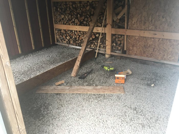 Grävt och grusat område med påbörjad gjutform för platta inne i ett bygge, verktyg syns på gruset.