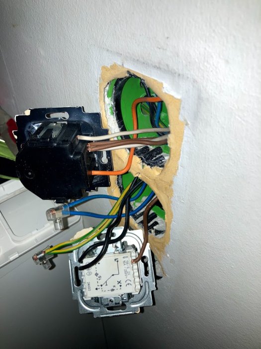 Elektrisk installation med en svart dimmer och en vit trappbrytare synliga i ett vägguttag med exponerade kablar.