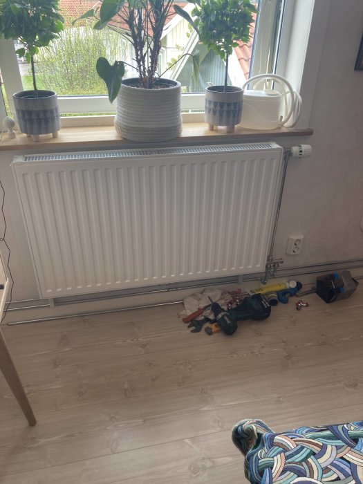 Nyinstallerad vit radiator (1000*500) under ett fönster med växter, verktyg syns på golvet.