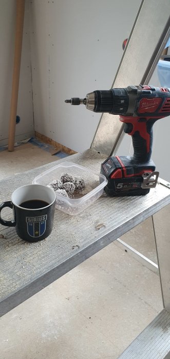 Borr och kaffekopp på arbetsplats med vägg av gips i bakgrunden.