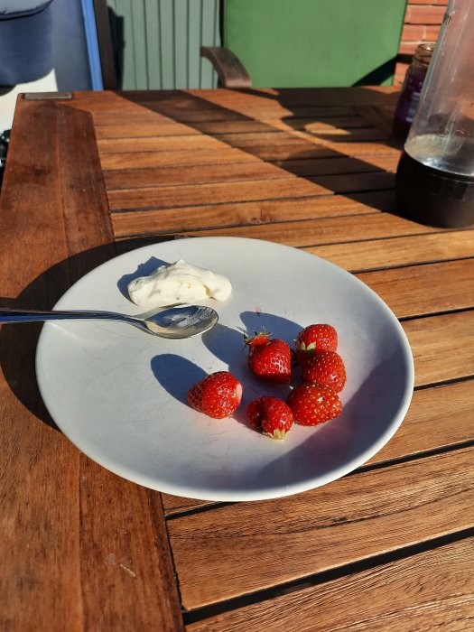 En tallrik med jordgubbar och grädde på ett träbord utomhus.