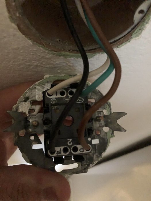 Någons hand håller en delvis installerad elektrisk strömbrytare med lösa kablar i en vägg.