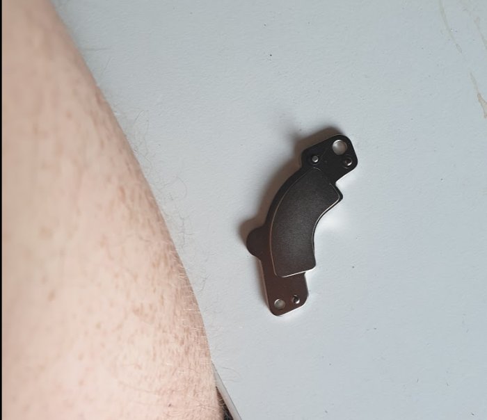 Neodyniummagnet från en gammal hårddisk ligger på ett vitt bord nära en persons arm.