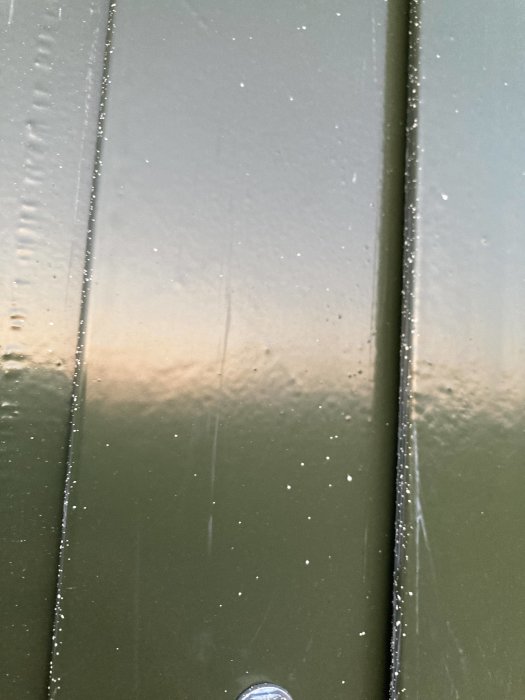 Nymålad mörkgrön metall med färgstänk, närbild på fönster- eller dörrkarm.