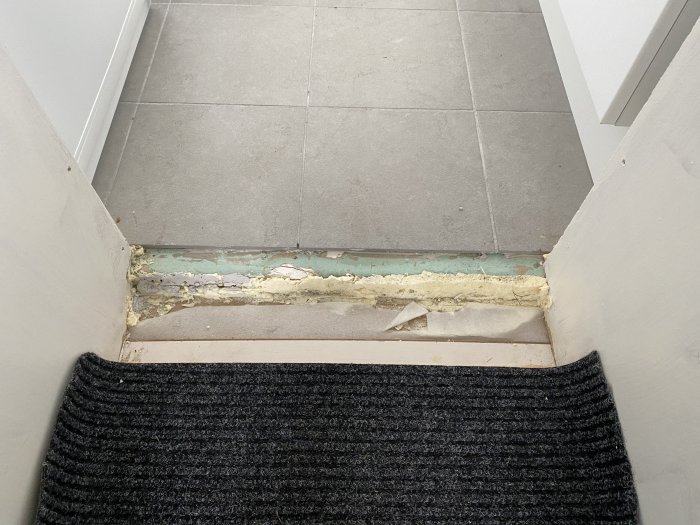 Glipa mellan klinkergolv i kök och passage till sovrum, med synlig nivåskillnad och skador.