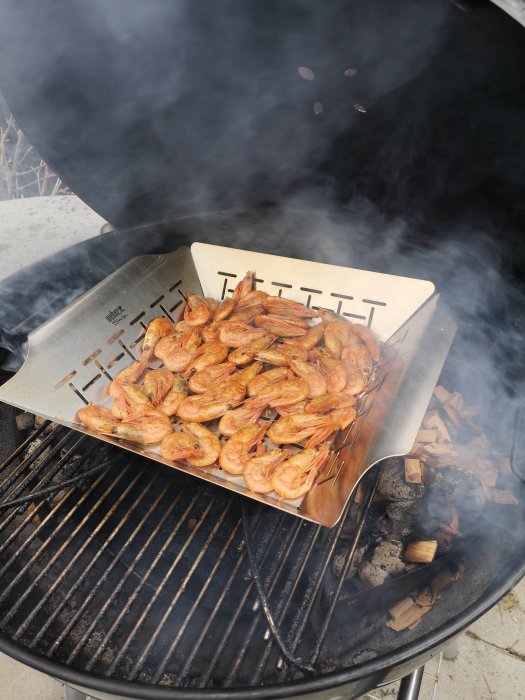 Räkor som röks på en grill med träflis och synlig rök, redo för fredagsmys.