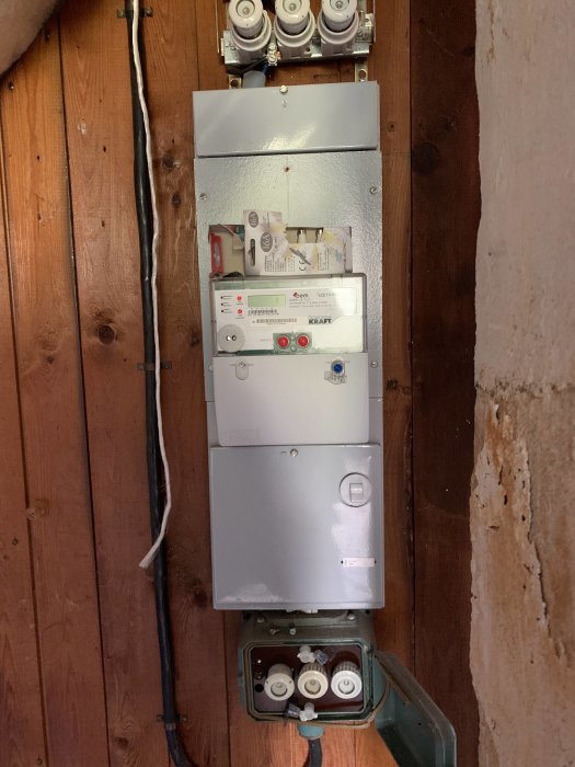 Elektrisk säkringsskåp med öppet dörr och flera säkringar på en trävägg.