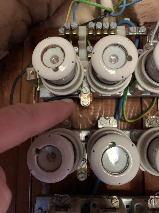 En hand pekar på en elektrisk säkringsbox med flera säkringar, varav de övre saknar ström.