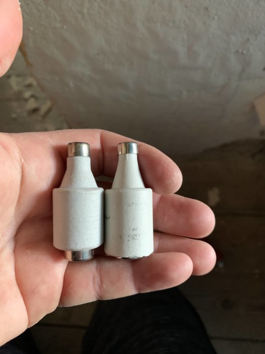Två vita säkringar med märkningen 16 hålls upp i en hand, en ser något större ut än den andra.