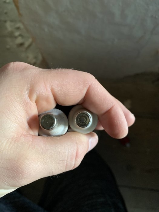 Hand håller två säkringar jämfört för storleksjämförelse, med fokus på topparna där en säkring är märkt med 16.
