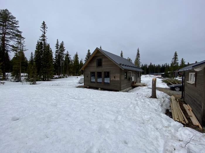 Nybyggt hus omgivet av snö med omgivande träd och molnhimmel.